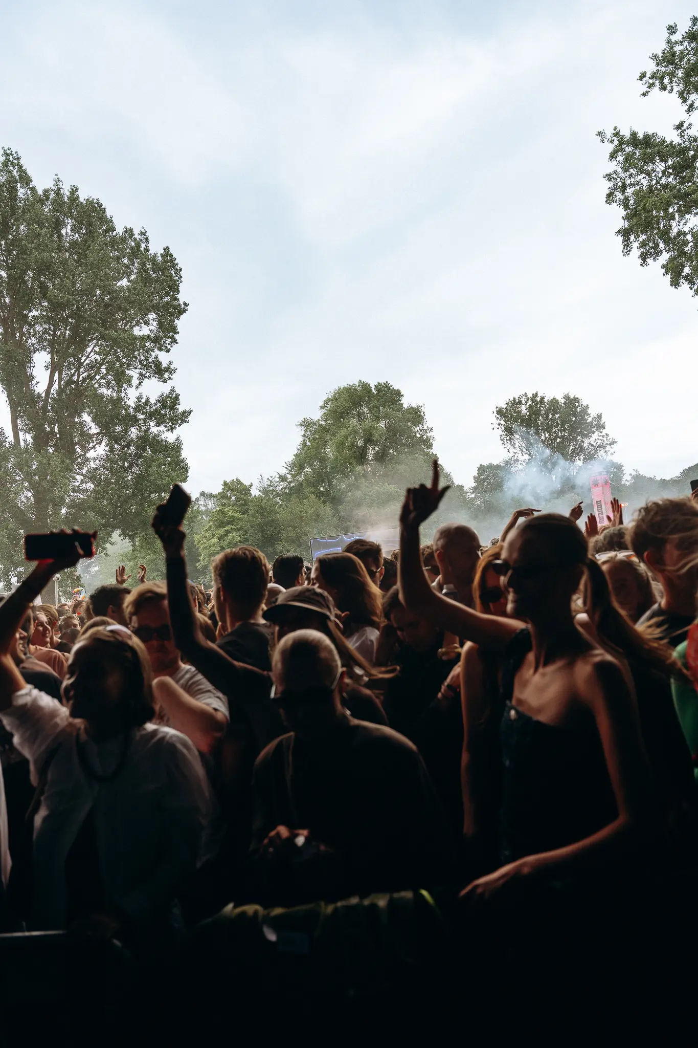 Festival fans with their hands in the air in front of a stage among the trees
