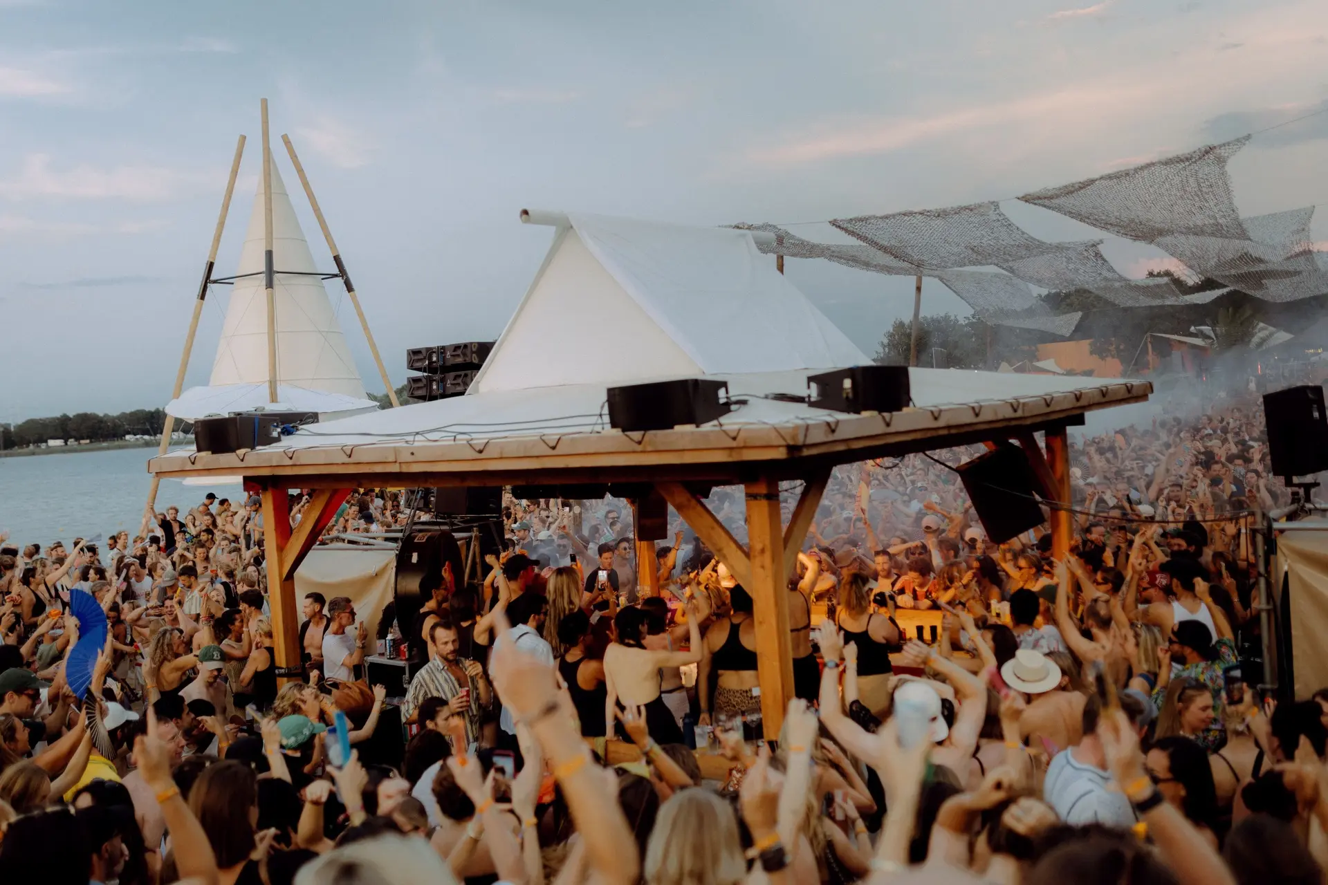 A crowd dancing in front of Lago Lago’s lakeside stage beneath white tents