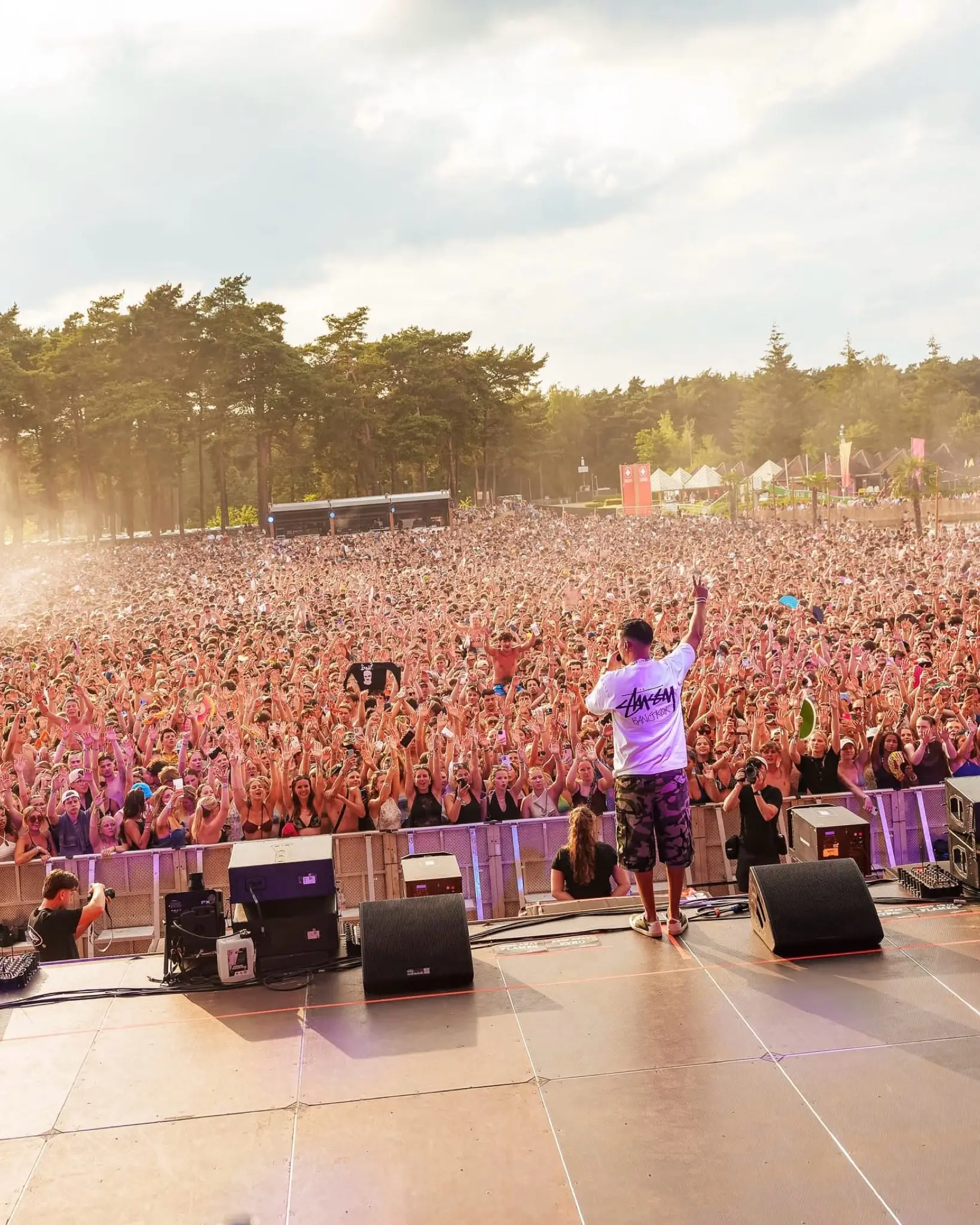 An artist on stage with his arm raised in front of a huge crowd at Sunrise Festival